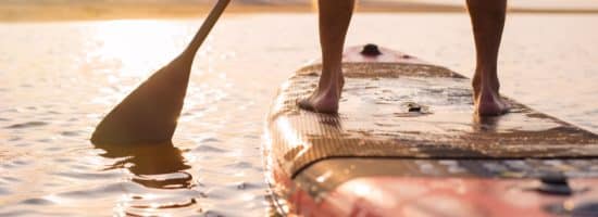 A person stands on a paddleboard at sunset