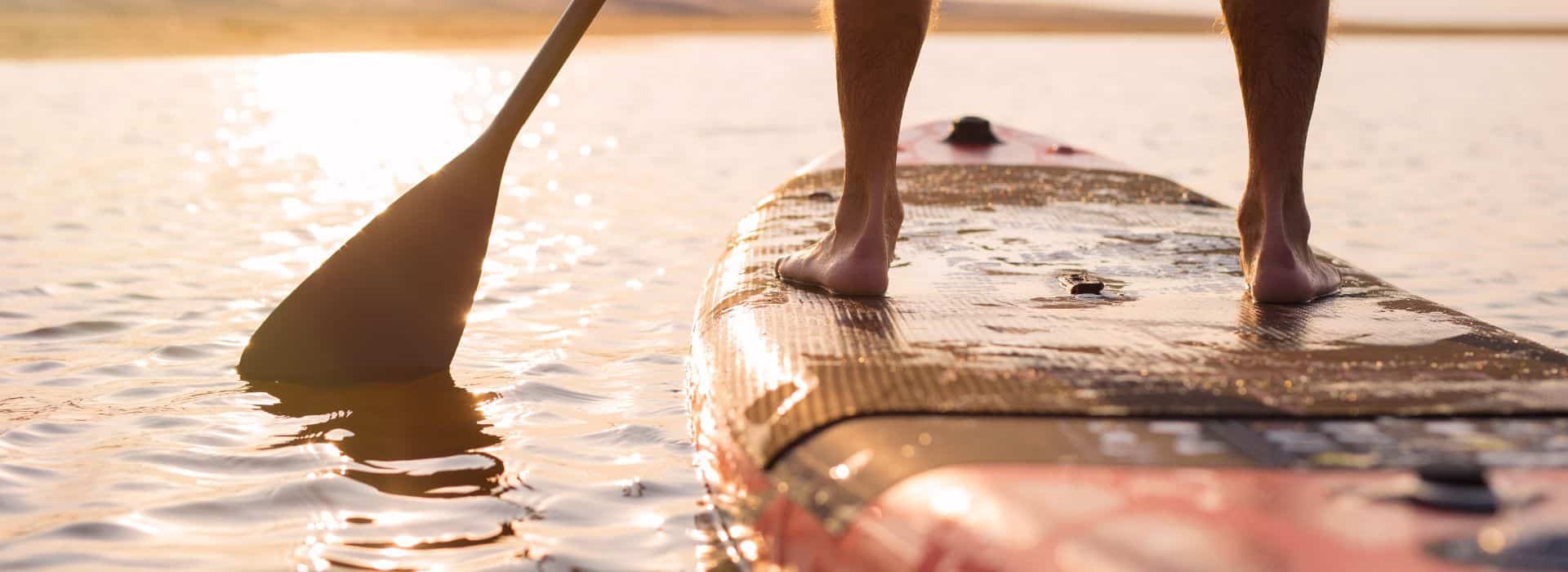 A person stands on a paddleboard at sunset