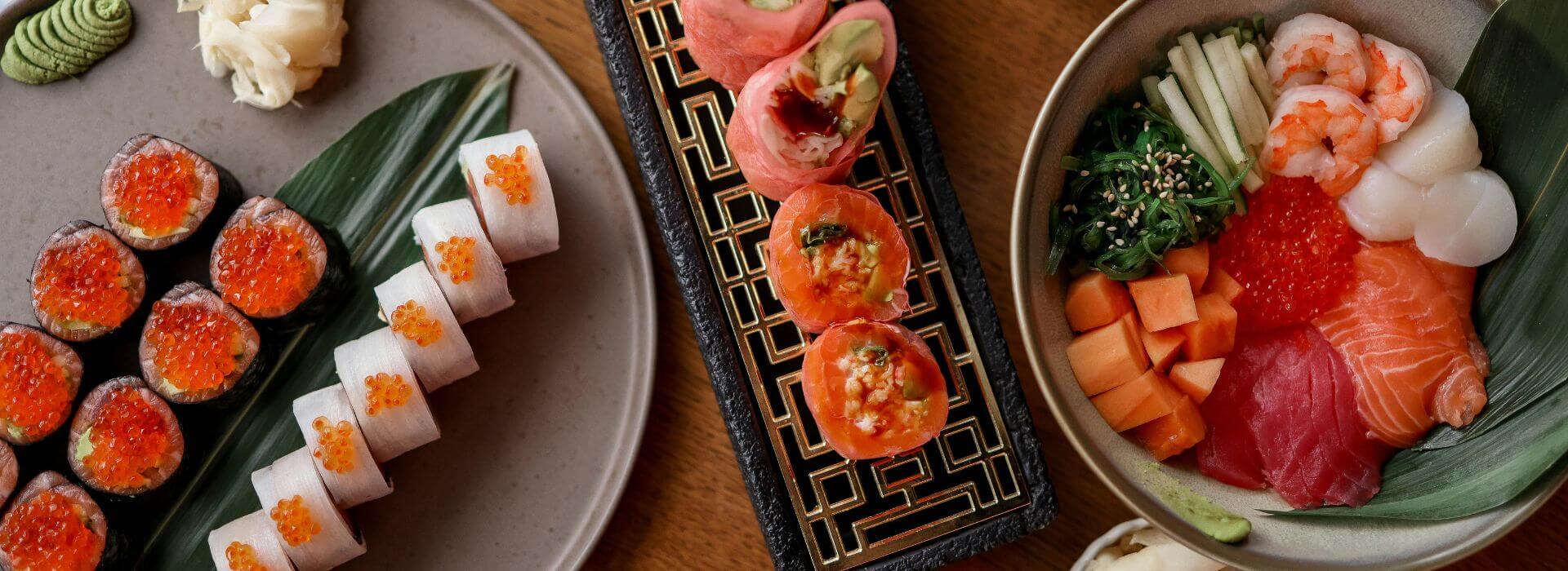 Assortment of sushi rolls and a sashimi bowl with salmon, tuna, shrimp, roe, cucumber, and seaweed.