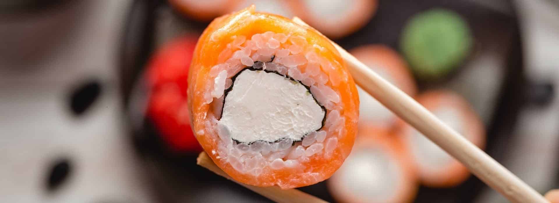 Sushi plate with sushi rolls and one held up close with chop sticks