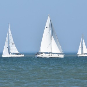 Three large all white sailboats together on crystal waters with a bright blue sky