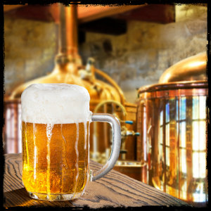 Glass of beer on a table next to copper brewing tanks