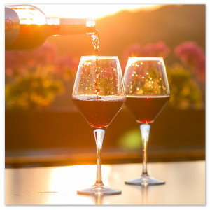 A bottle of red wine pouring into two glasses on a table. Photo by photo-nic-co-uk-nic- www.unsplash.com