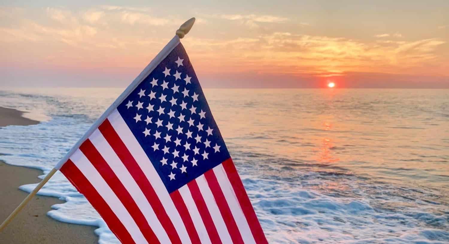 American flag on a pole with the ocean in the background and the sun starting to come up