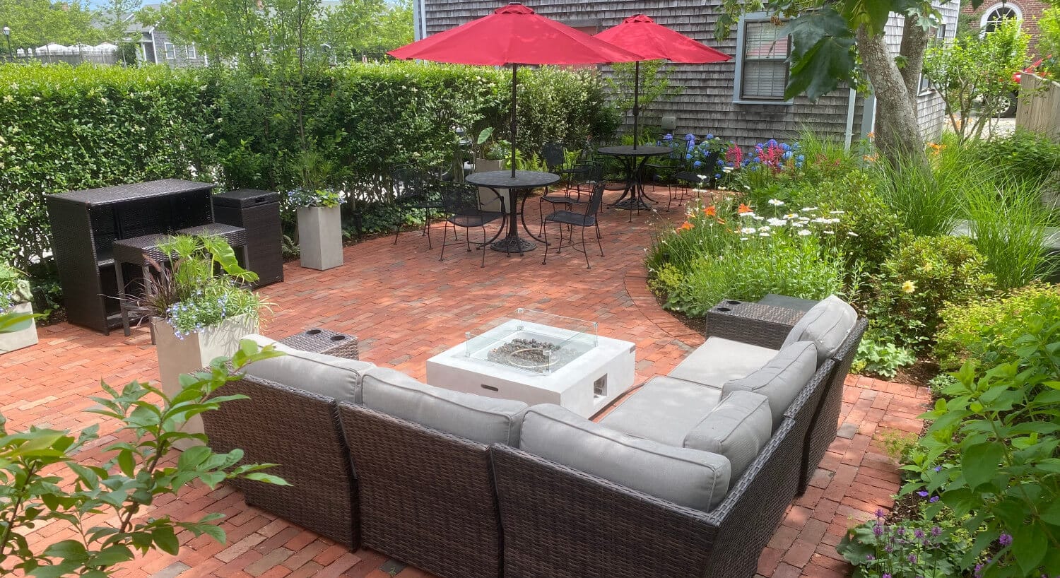 Exterior view of the property with large red brick patio with patio tables,chairs, wicker sectional, and fire pit surrounded by privacy shrubs, plants, and trees