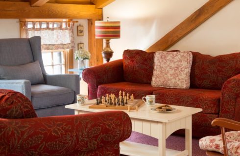 Sitting area with upholstered sofas in a dark red patterned fabric and an arm chair in a blue denim fabric surrounding a light wooden coffee table