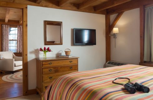 Bedroom with multicolored striped bedspread, wooden dresser, flat-screen TV, and view into the next room