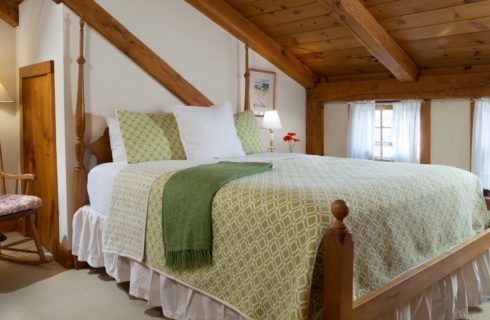 Bedroom with wooden bed, white linens, white and green bedspread, and wooden rocking chair