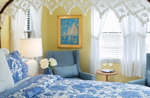Bedroom with yellow walls, dark wooden four-poster bed, blue and white paisley bedding, denim upholstered arm chairs