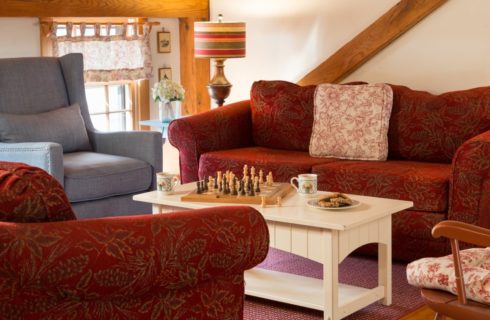 Sitting area with upholstered sofas in a dark red patterned fabric and an arm chair in a blue denim fabric surrounding a light wooden coffee table