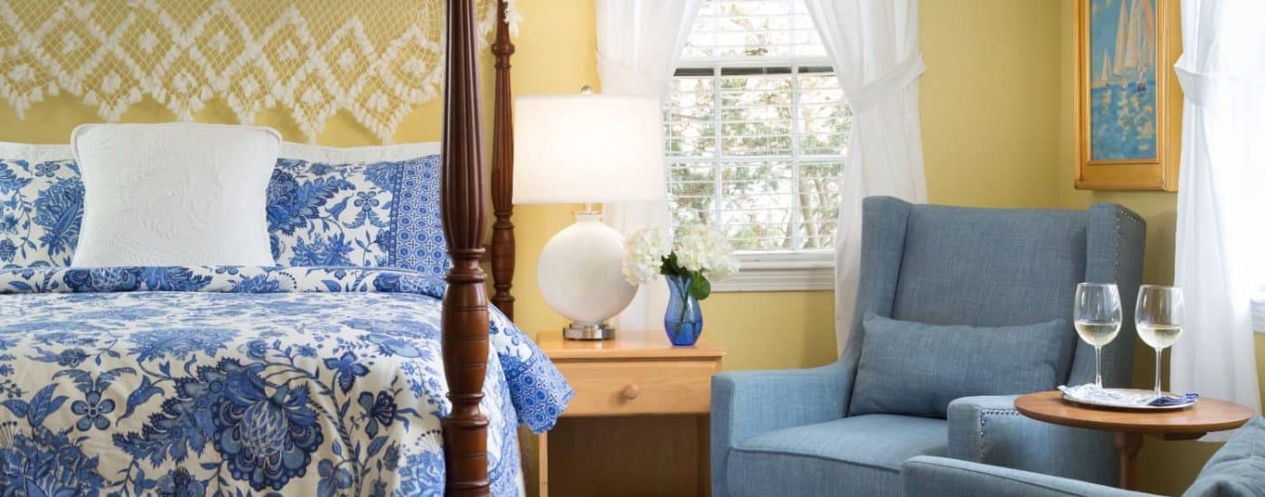 Bedroom with yellow walls, dark wooden four-poster bed, blue and white paisley bedding, denim upholstered arm chairs