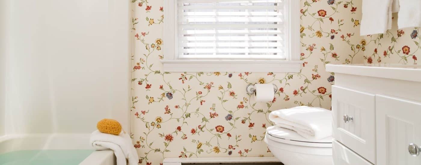 Bathroom with multicolored floral wall paper, white tile flooring, white wooden vanity, tub, and shower