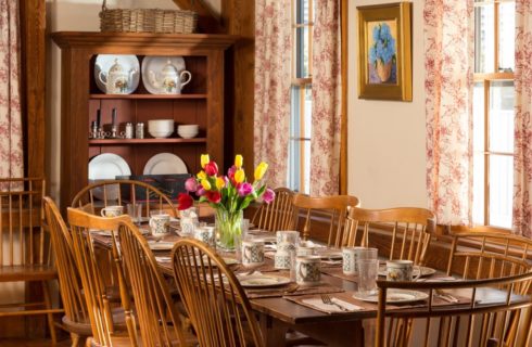 Dining room with a dark wooden china hutch and large wooden table and chairs with red, yellow and purple tulips in a vase on top