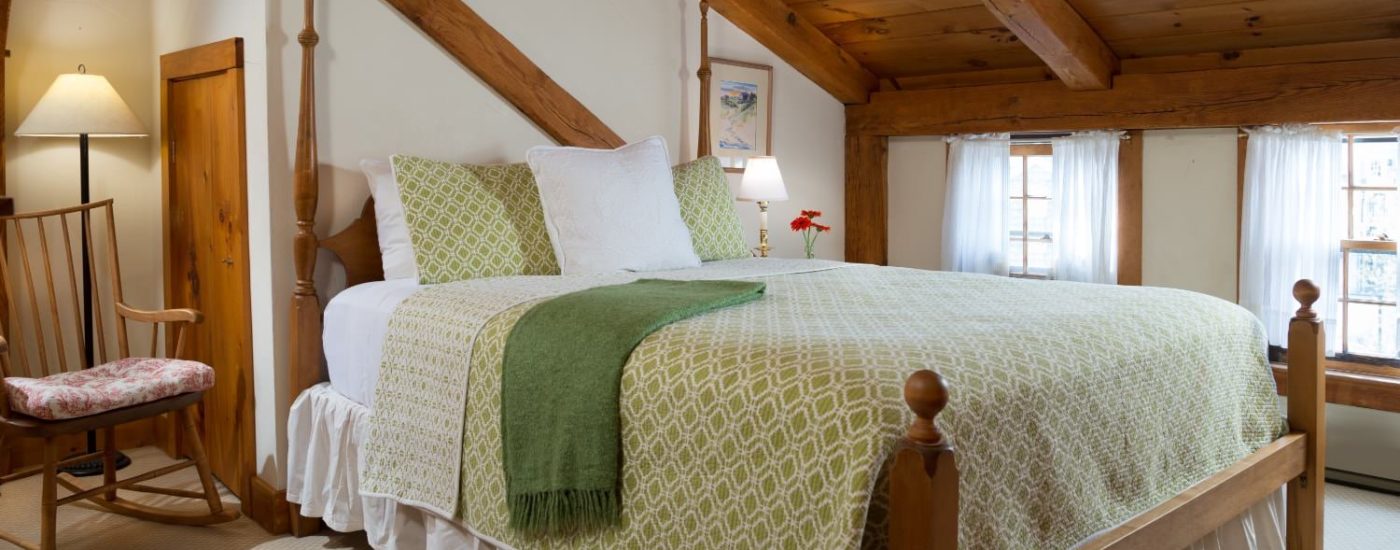 Bedroom with wooden bed, white linens, white and green bedspread, and wooden rocking chair