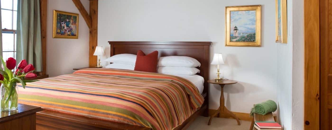 Bedroom with dark wooden headboard, white linens, multicolored striped bedspread, and wooden side tables with lamps