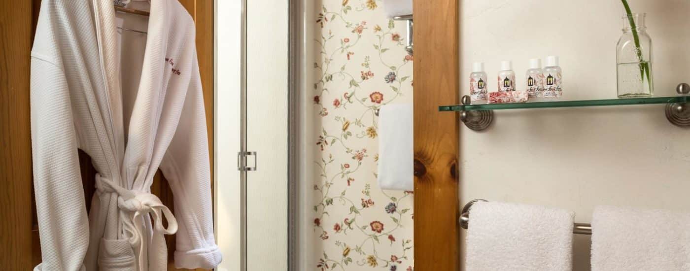 Bathroom with glass shelf, towel bar, hanging white robe, and separate area with stand up shower
