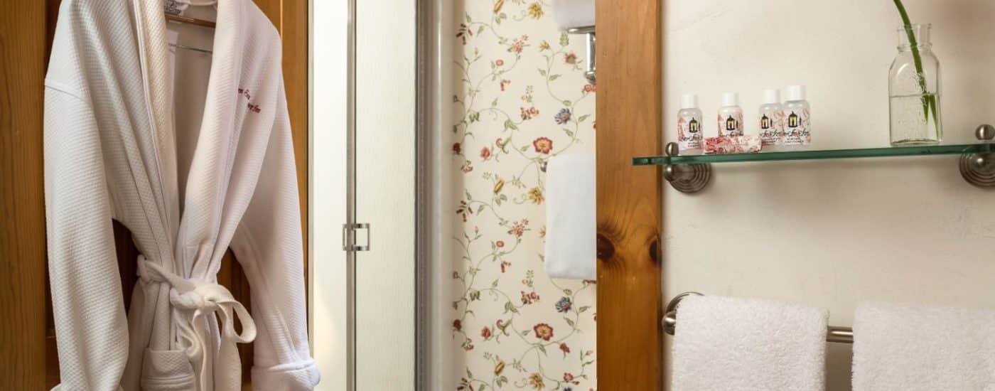 Bathroom with glass shelf, towel bar, hanging white robe, and separate area with stand up shower