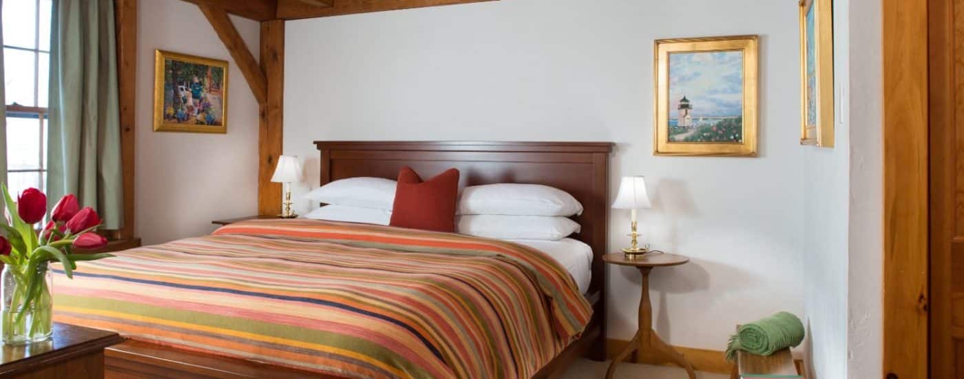 Bedroom with dark wooden headboard, white linens, multicolored striped bedspread, and wooden side tables with lamps