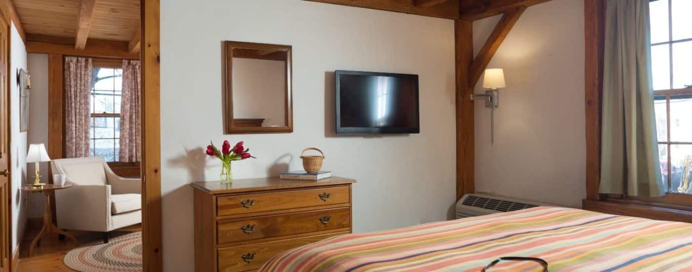 Bedroom with multicolored striped bedspread, wooden dresser, flat-screen TV, and view into the next room