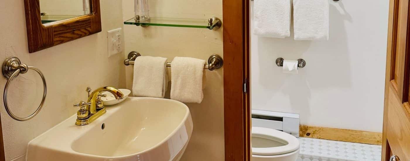 White pedestal sink with mirror, glass shelf and hanging towels and separate toilet room.