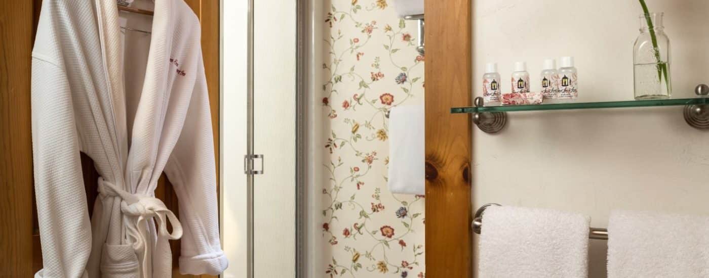 Bathroom with glass shelf, towel bar, hanging white robe, and separate area with stand up shower