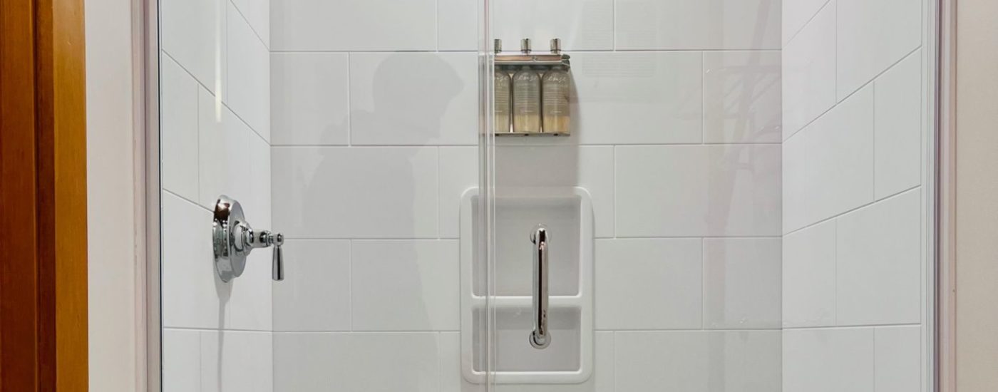 White tiled shower with hand bar, and toiletry bottles