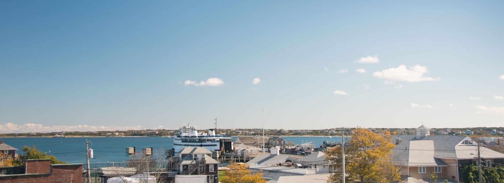 View of houses close to a wharf where a ferry is docked with water and a land mass with other houses near the water in the background