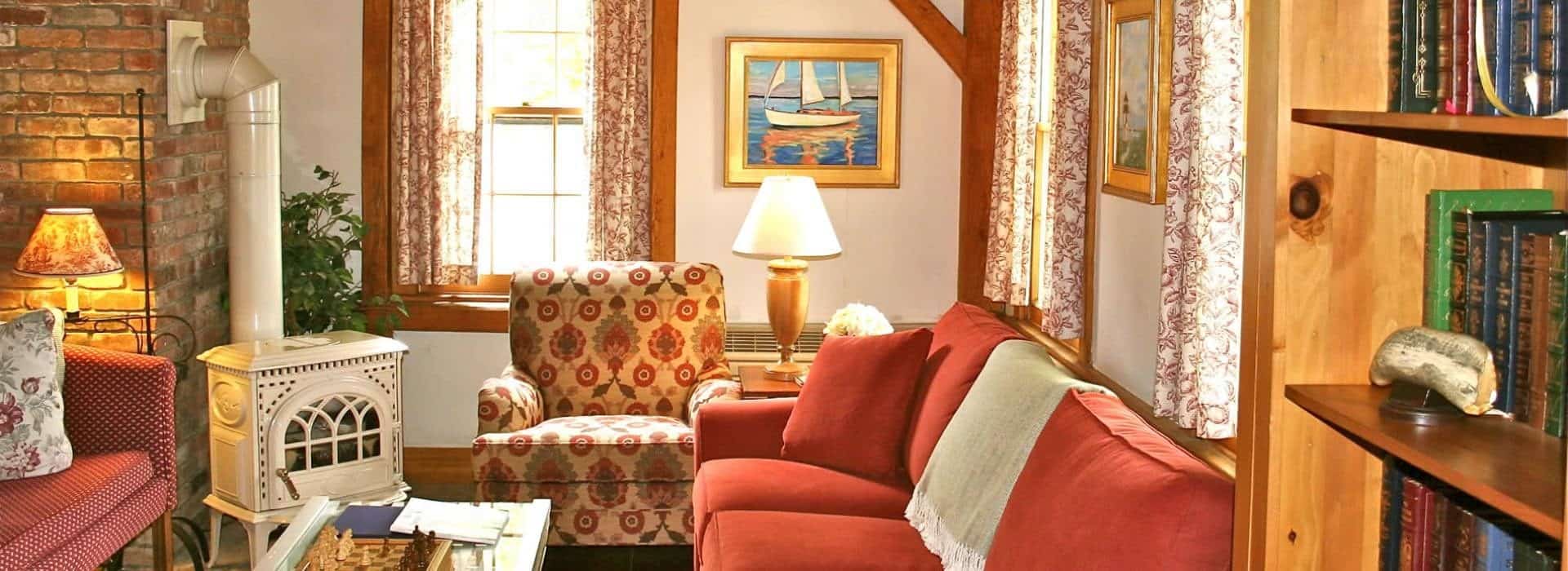 Living room with antique wooden fireplace, burgundy sofa, upholstered oversized armchair, and white wooden coffee table with glass top