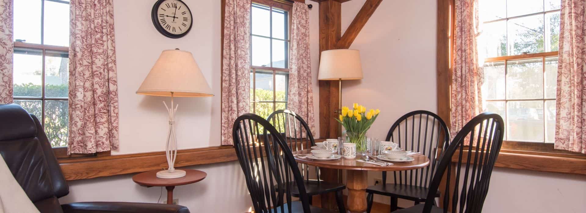 Dining area with a small wooden table with four black wooden chairs and a vase with yellow tulips on top of the table