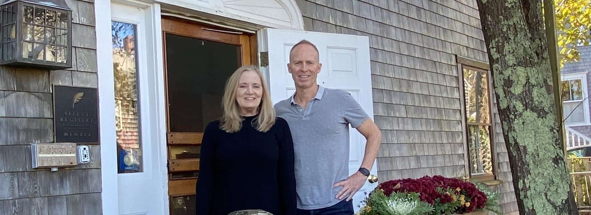 Lady with navy top and man with gray polo standing at the front entrance of the property