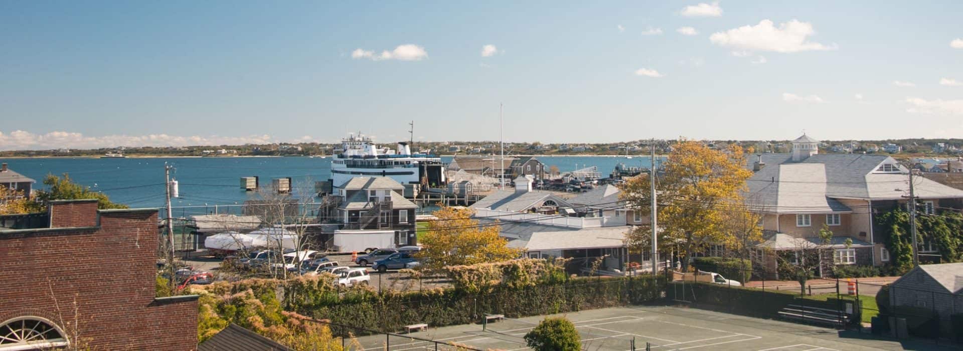 View of houses close to a wharf where a ferry is docked with water and a land mass with other houses near the water in the background