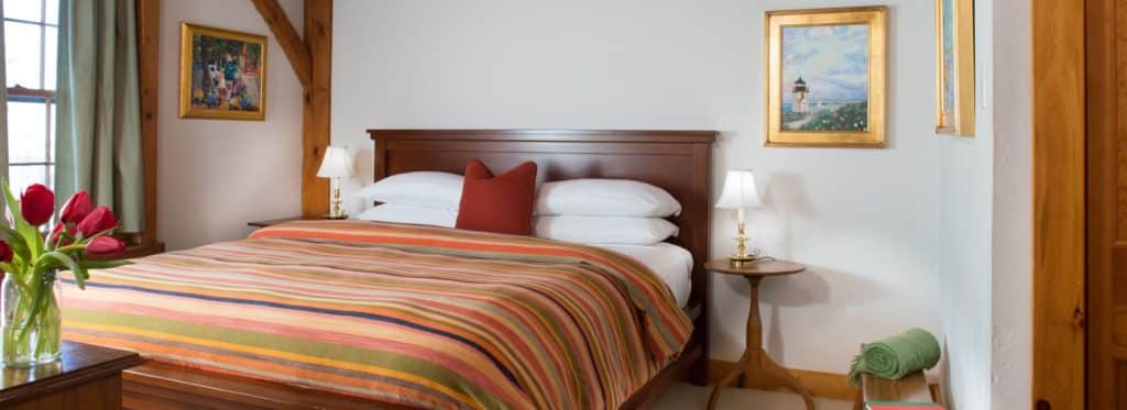 Bedroom with dark wooden headboard, white linens, multicolored striped bedspread, and wooden side tables with lamps