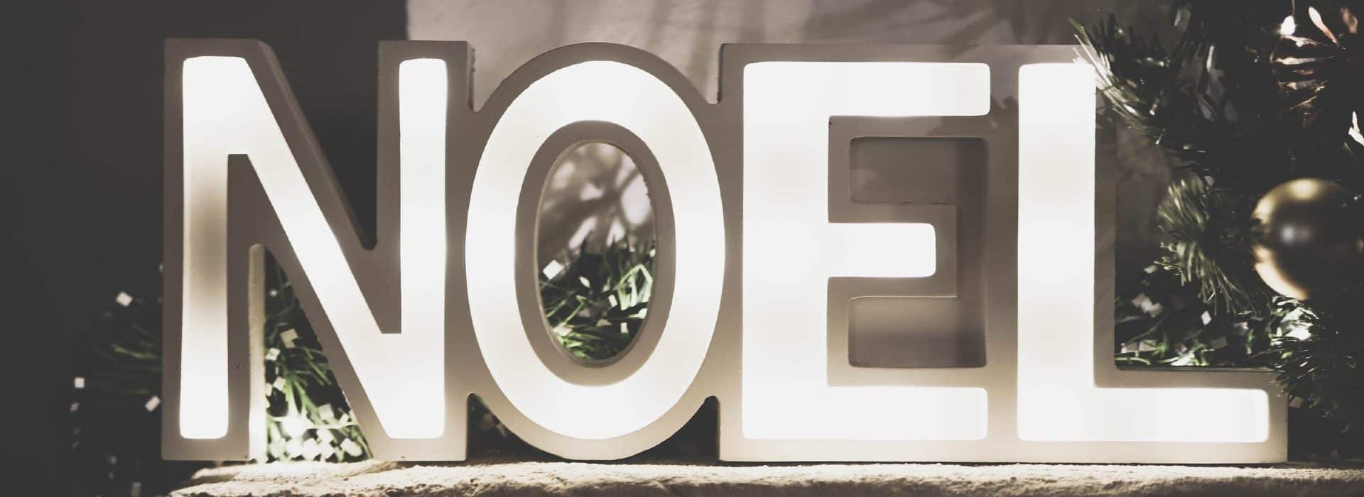 Black and white tone with the letters noel lit up with christmas tree branches behind