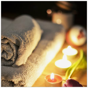 Two tan towels rolled up next to several lit pink candles and a flower