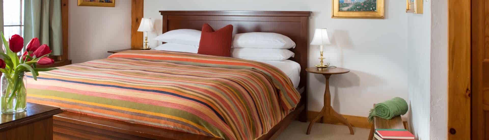 Bedroom with dark wooden headboard, white linens, multicolored striped bedspread, and wooden side tables with lamps