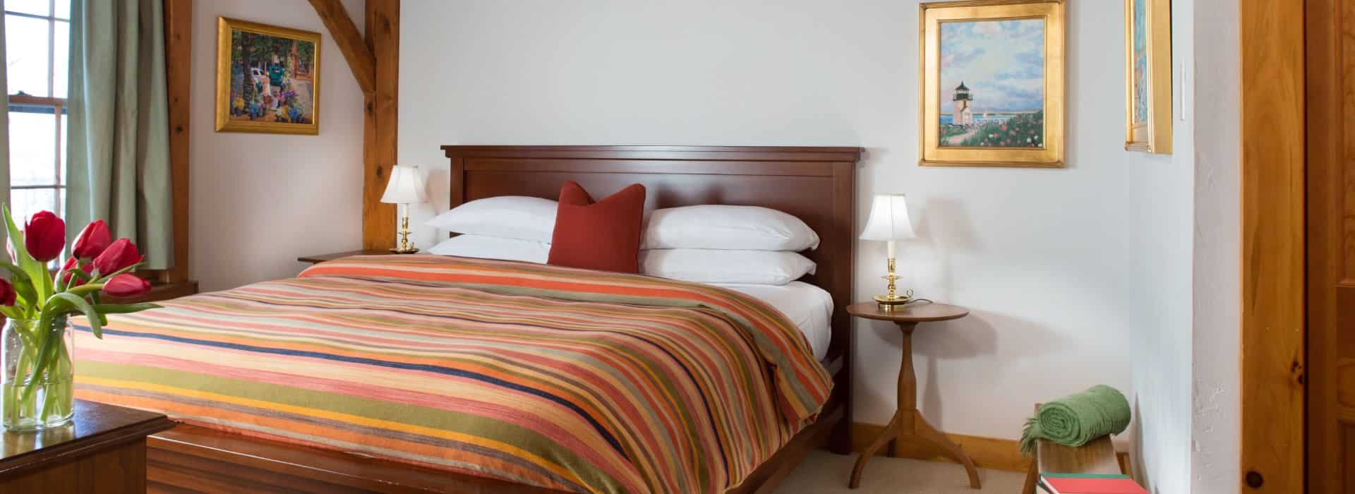 Bedroom with dark wooden headboard, white linens, multicolored striped bedspread, and wooden side tables with lamps