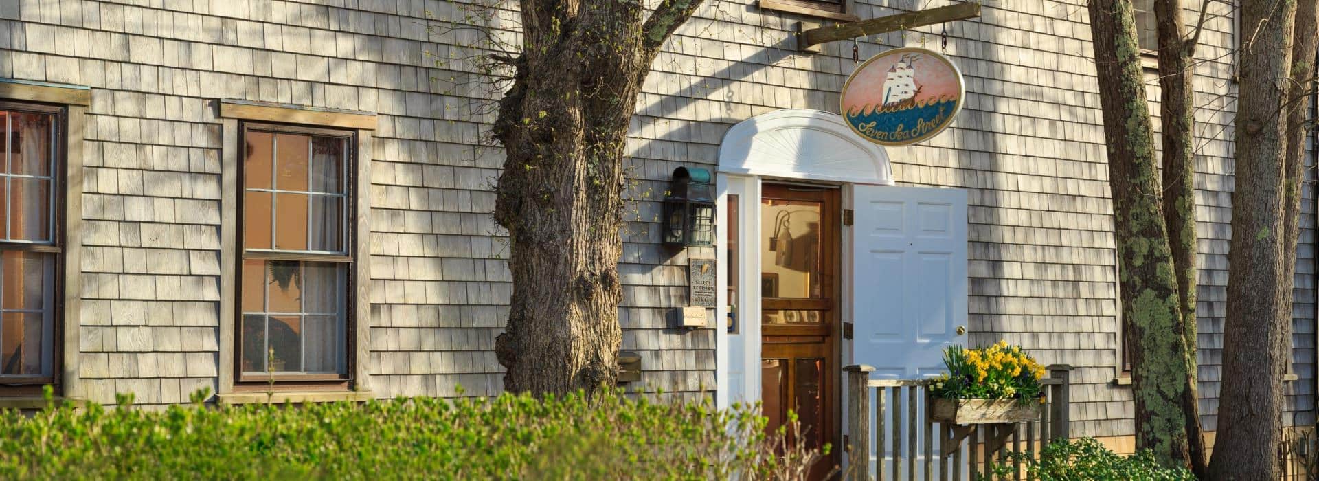 Front exterior view of the property with cedar shake siding, white painted door, and green shrubs