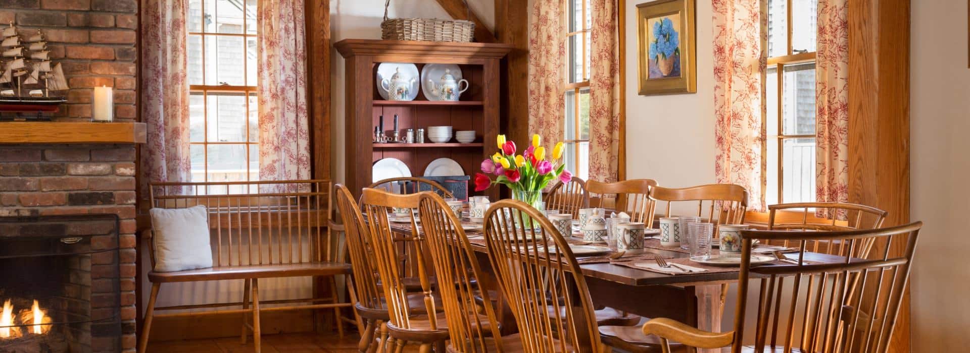 Dining room with brick fireplace and large wooden table and chairs with red, yellow and purple tulips in a vase on top