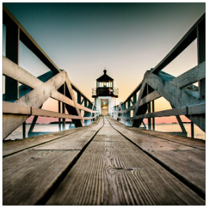 White lighthouse at the end of a long wooden boardwalk at dusk